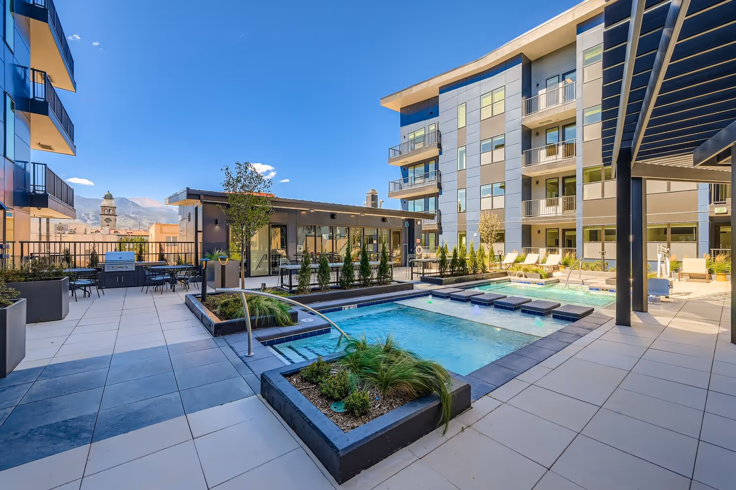 Outdoor pool and sundeck with a view of the resident clubhouse and a grilling station at Avian Apartments in Colorado Springs, CO.