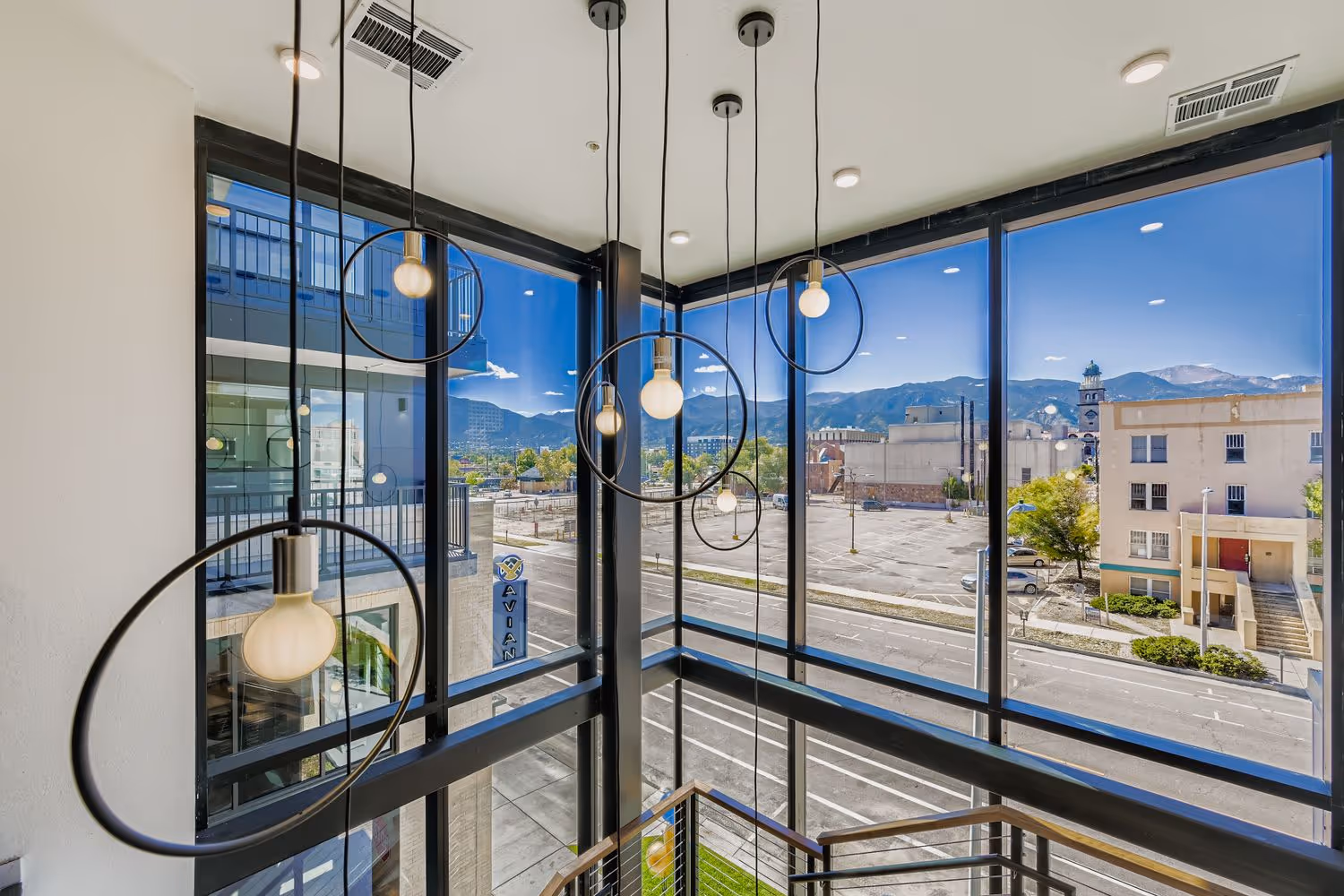 Two-story staircase and multi-level windows with modern light fixtures, offering panoramic views of the city and Pikes Peak at Avian in Colorado Springs, CO.