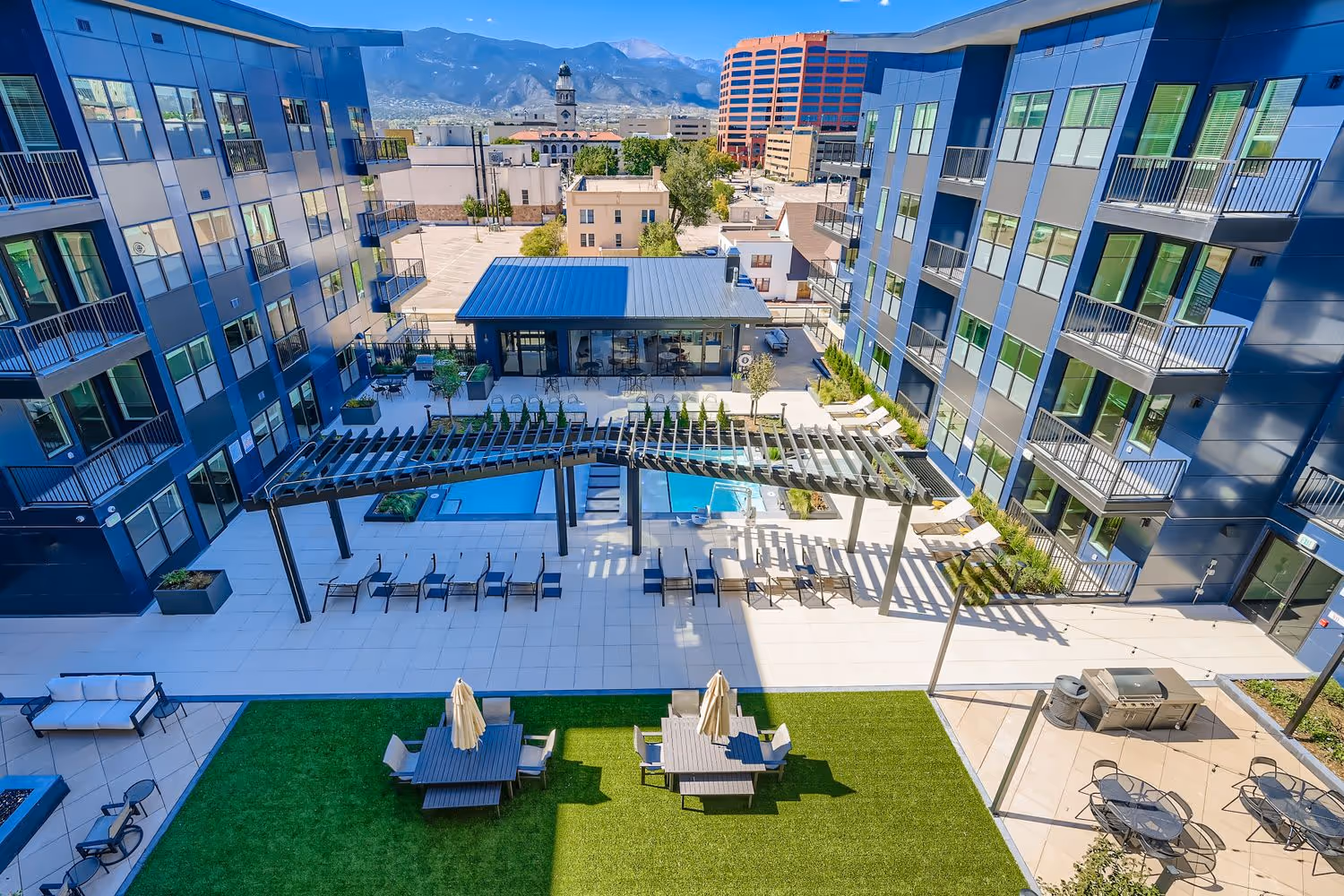 Aerial view of the modern Avian apartment buildings, showing the courtyard pool, sun deck, and outdoor grilling area with Pikes Peak in the background in Colorado Springs, CO.